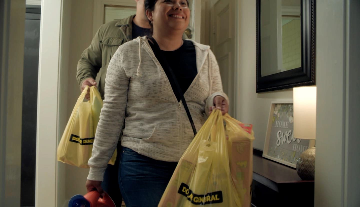 Woman and man enter a home with filled Dollar General shopping bags.